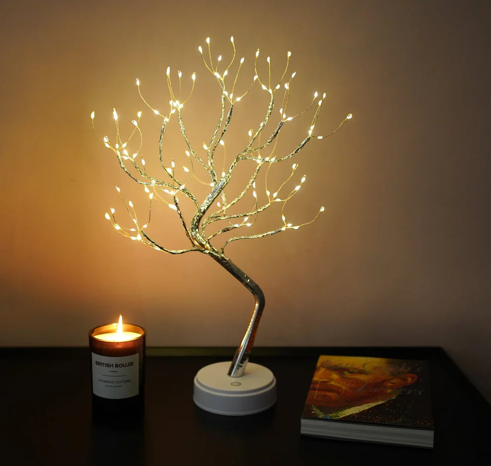 Decorative LED tree on a table with a candle and book in the background